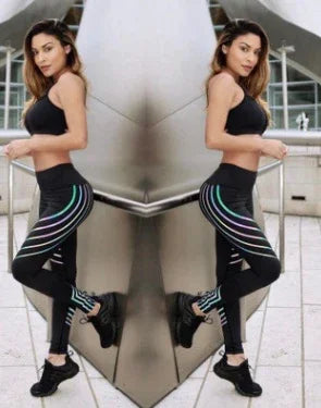 Fit woman in black sports bra and colorful striped leggings posing in urban modern setting
