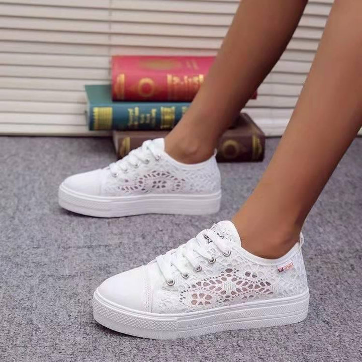 White lace casual sneakers worn on feet on gray carpet with stacked books in background