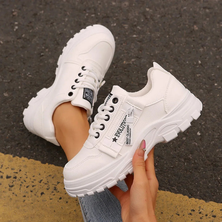 White chunky platform sneakers with black eyelets and zipper detail worn on asphalt road with yellow line