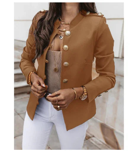 Woman wearing brown military-style blazer with gold buttons, layered necklaces, and white pants