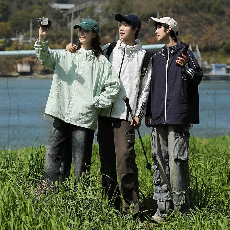 Three young hikers in casual jackets and caps taking photos by riverside in grassy outdoor setting
