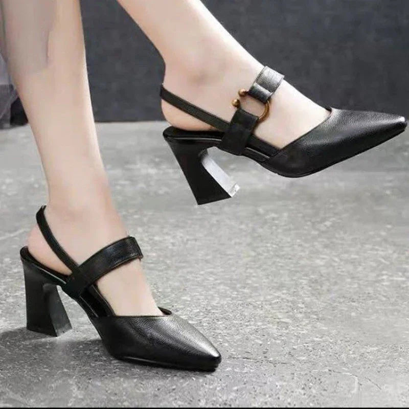 Close-up of black pointed-toe slingback heels with block heels and gold buckle detail on gray floor