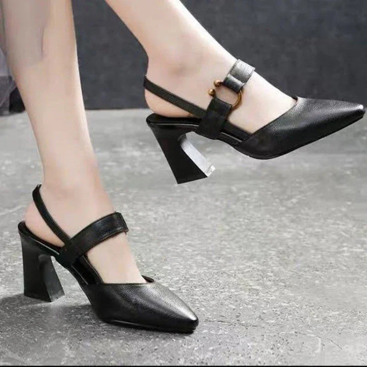 Close-up of black pointed-toe slingback heels with block heels and gold buckle detail on gray floor