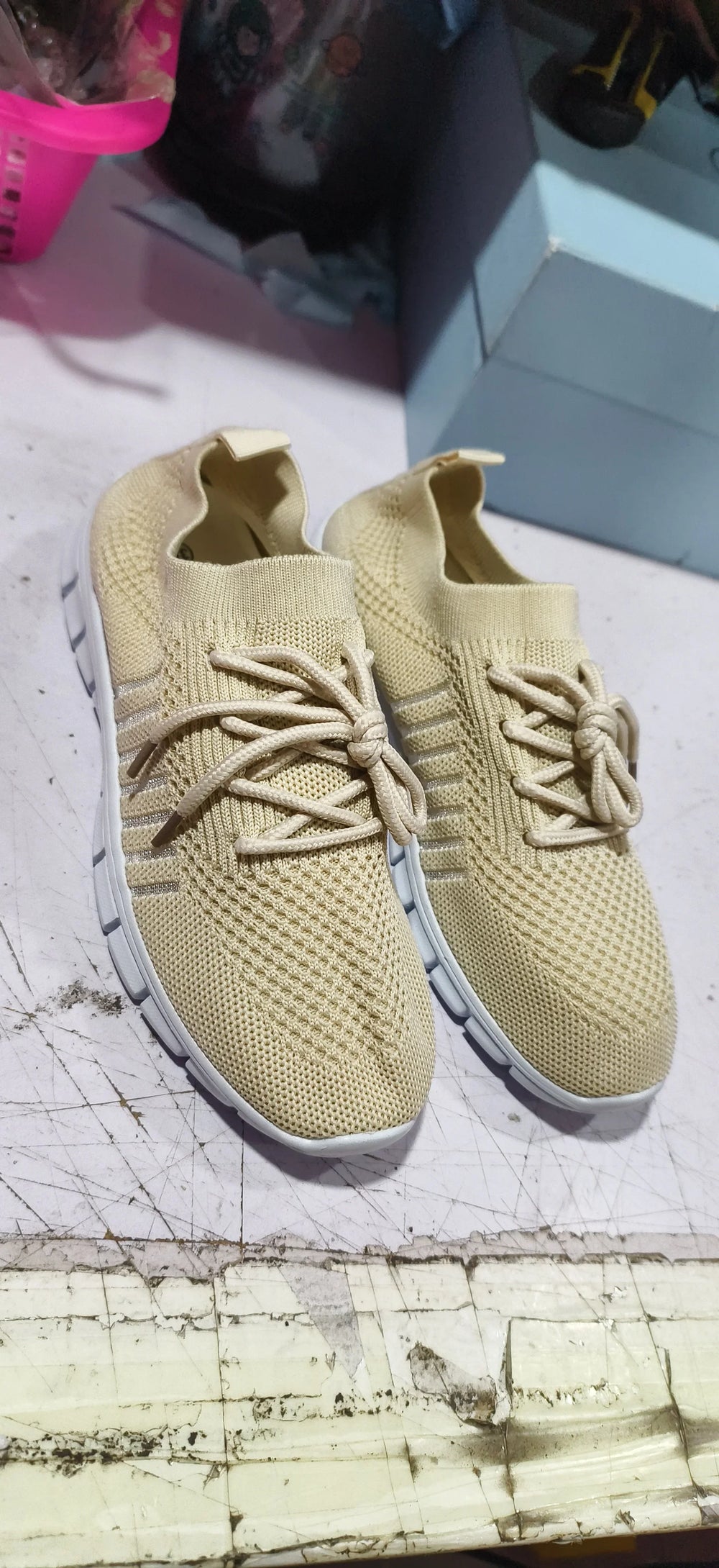 Pair of beige knitted sneakers with white soles on a scratched white surface