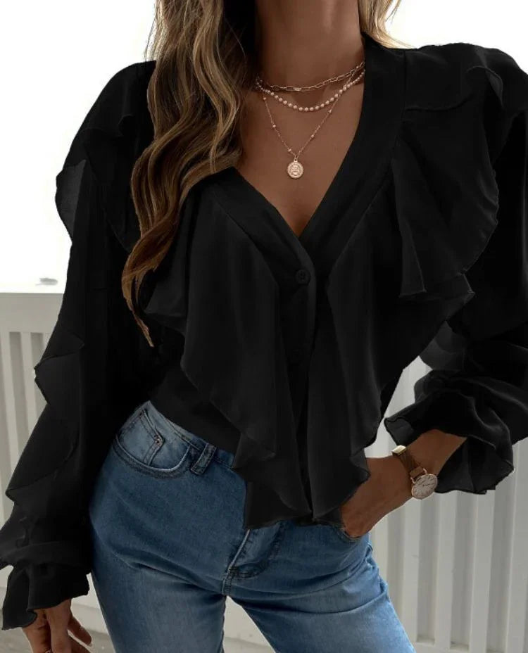 Woman wearing black ruffled blouse with V-neck and layered gold necklaces paired with blue jeans