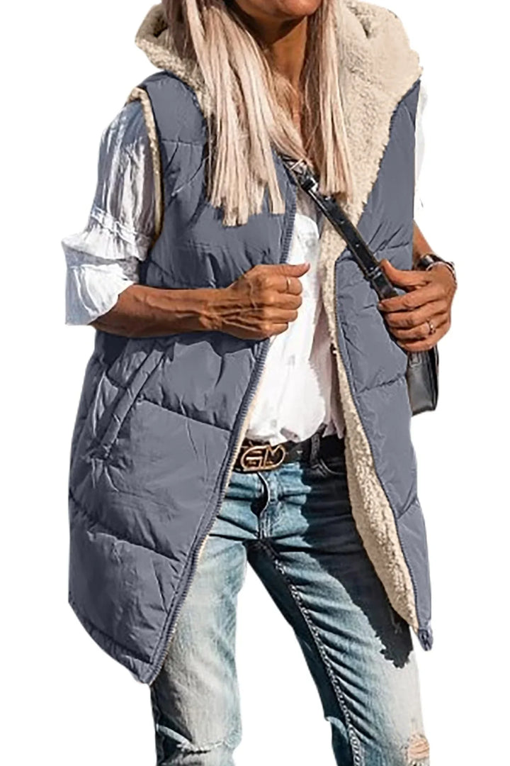 Woman wearing gray quilted sleeveless vest with sherpa lining over white blouse and distressed blue jeans
