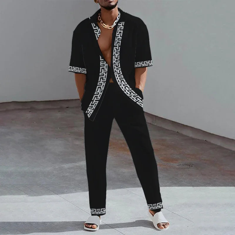 Man wearing black short-sleeve shirt and pants with white Greek key pattern, white sandals, and gold chain necklace
