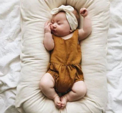 Sleeping baby in a mustard romper and cream headband on a cozy off-white cushion