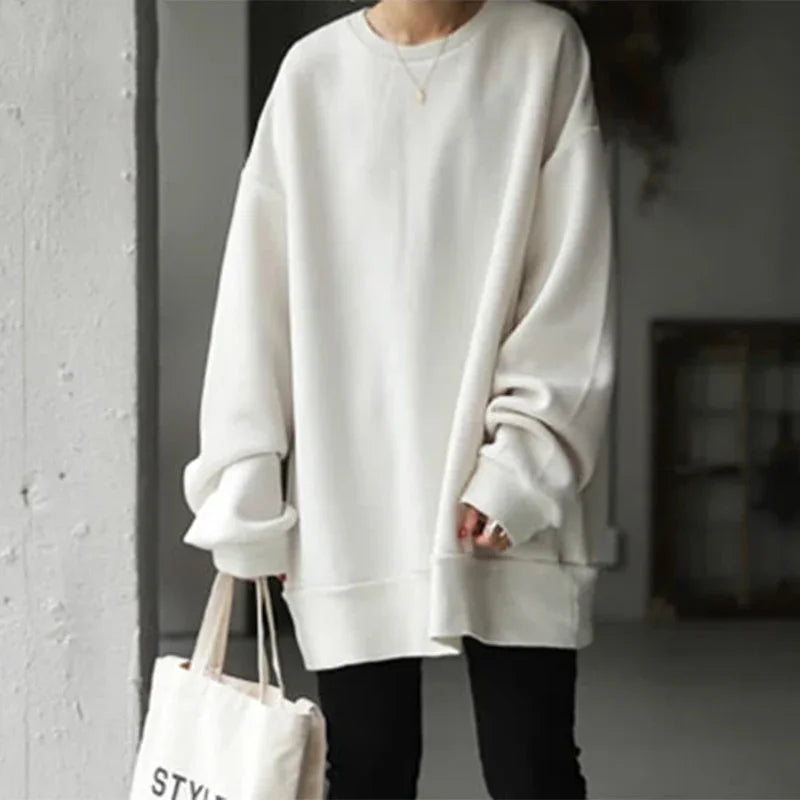 Person wearing oversized white sweatshirt with long sleeves and black pants holding cream canvas tote bag