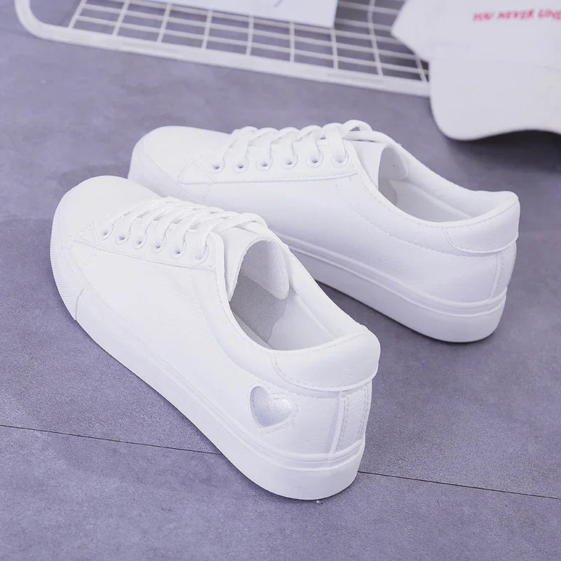 Pair of white low-top sneakers with heart detail on the heel, placed on gray surface