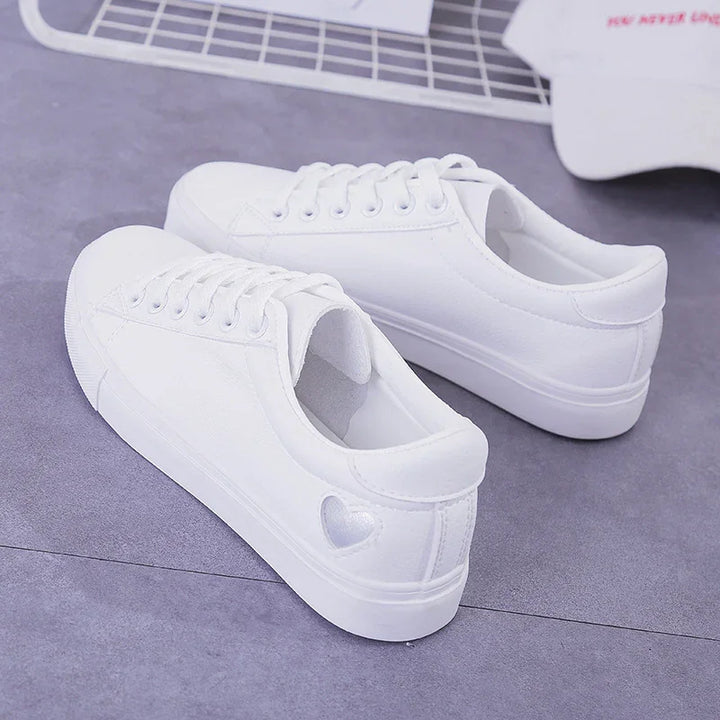 Pair of white low-top sneakers with heart detail on the heel, placed on gray surface