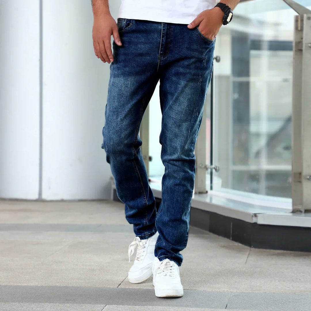 Man wearing dark blue faded jeans and white sneakers walking outdoors near glass railing