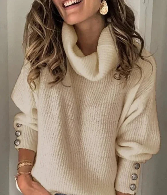 Woman wearing a cream-colored turtleneck sweater with button details on sleeves and gold earrings
