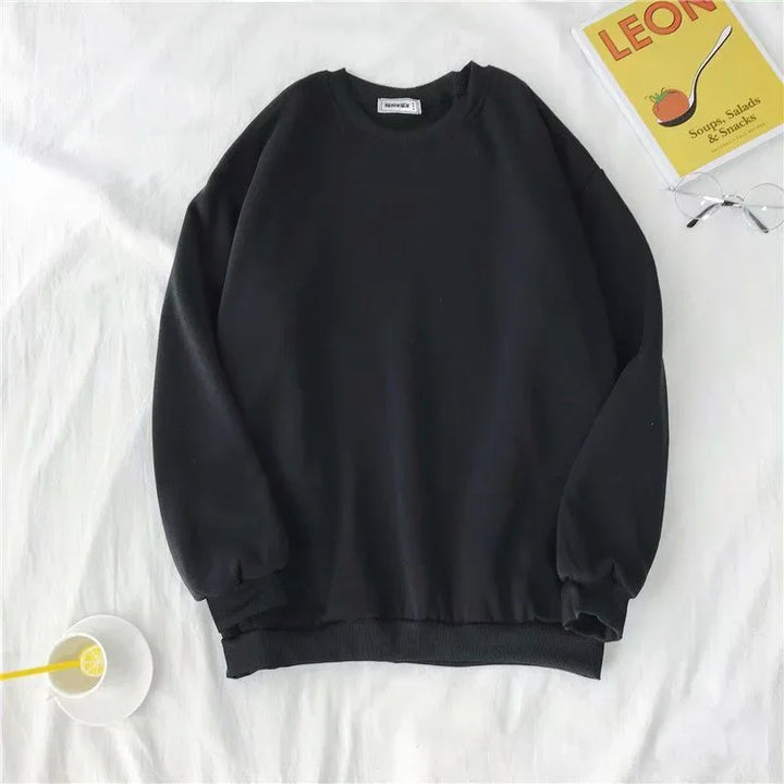 Black long-sleeve crewneck sweatshirt on white fabric background with glass, book, and cup