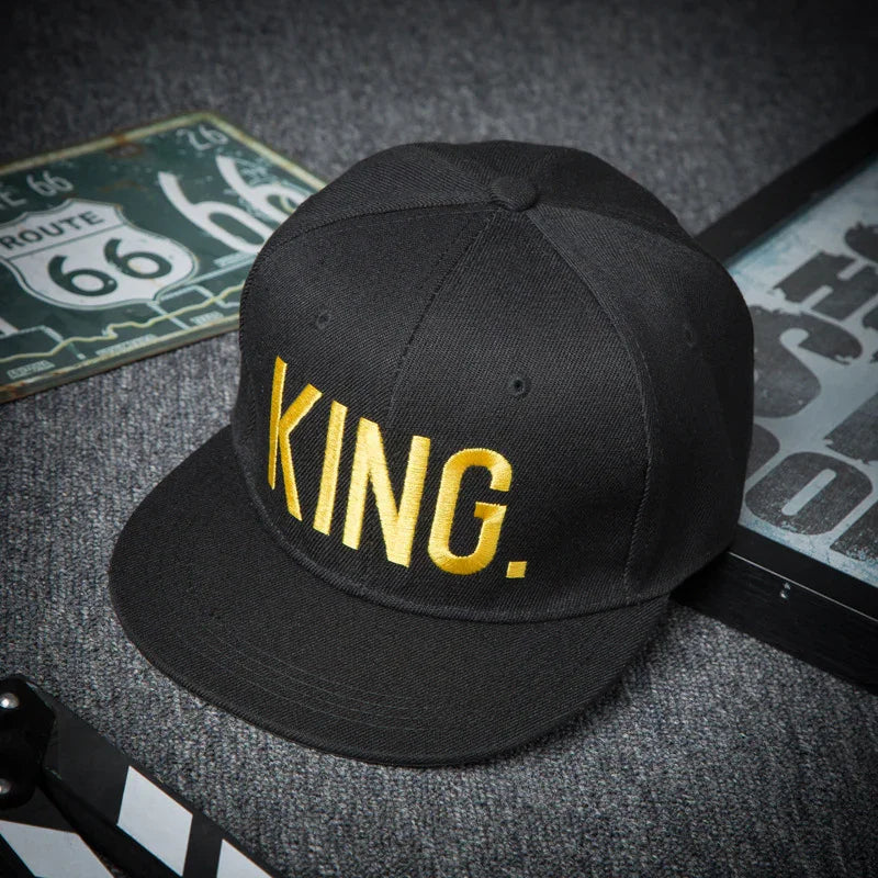Black snapback hat with gold embroidery spelling KING on gray carpet next to Route 66 signs