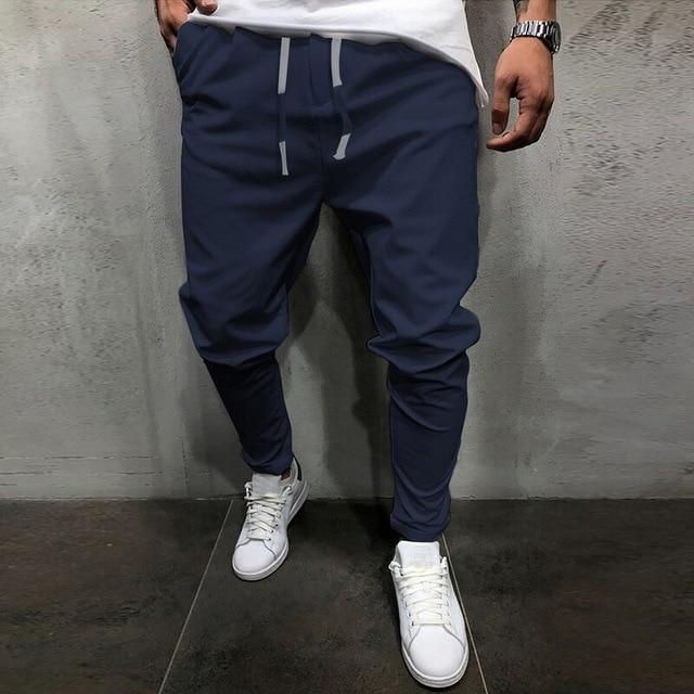 Man wearing navy blue casual jogger pants with drawstring and white sneakers against gray wall