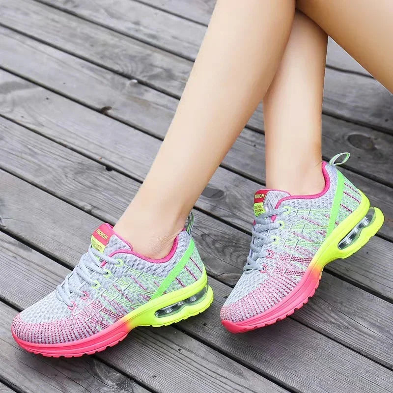 Colorful women's running shoes with pink, neon green, and gray knit design on wooden floor