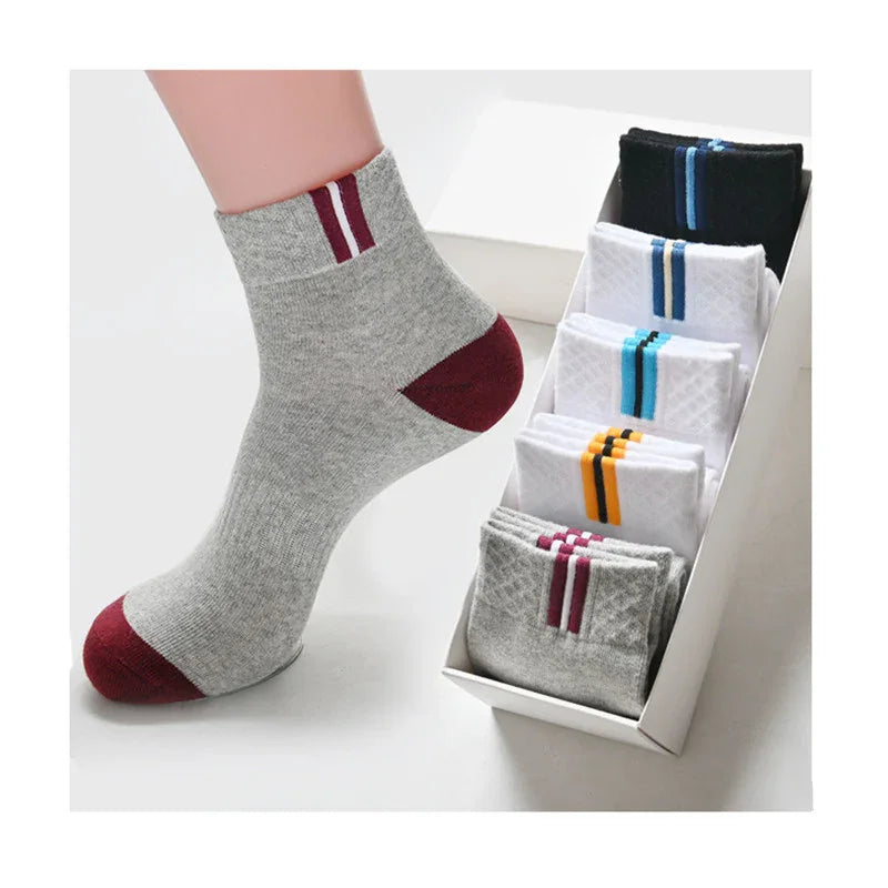 Gray ankle sock with burgundy toe and heel alongside a box of assorted striped socks in black, white, gray, and blue colors