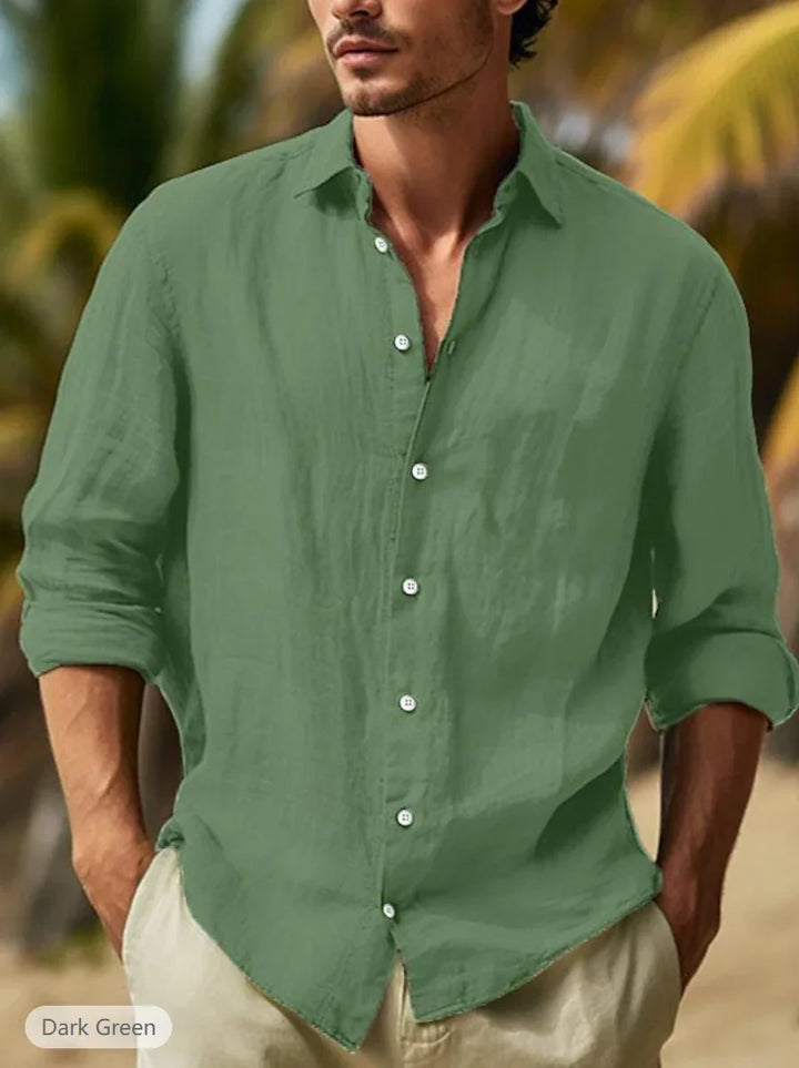 Man wearing casual dark green button-up linen shirt with rolled sleeves in outdoor tropical setting