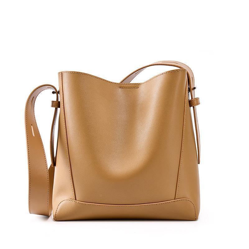 Minimalist tan leather bucket bag with adjustable strap on white background