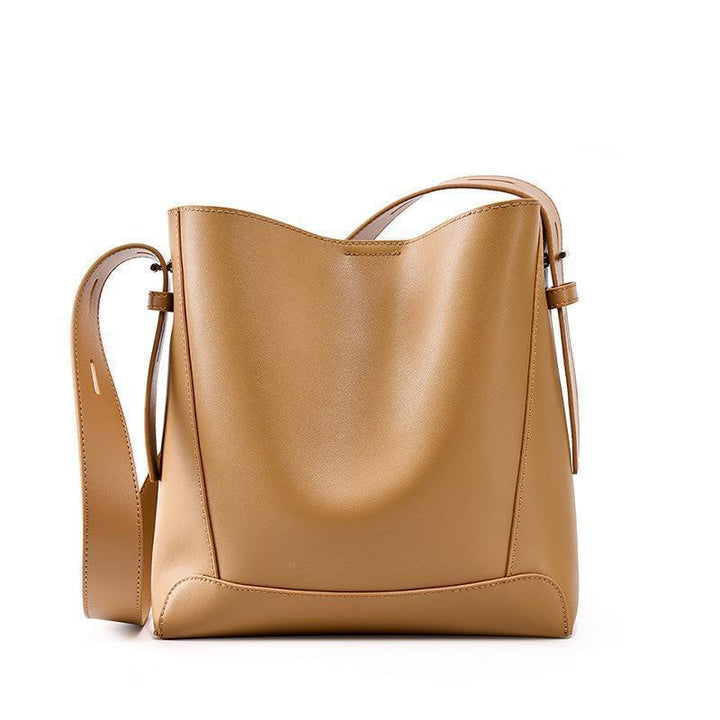 Minimalist tan leather bucket bag with adjustable strap on white background
