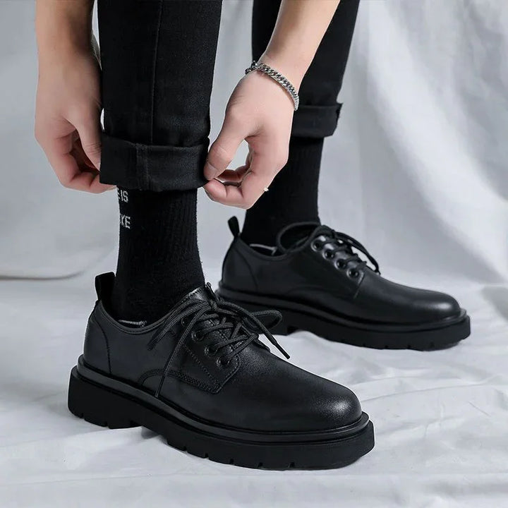 Black leather lace-up shoes with thick soles worn with black socks and rolled-up black pants
