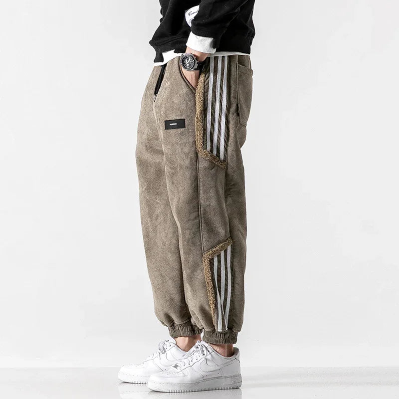 Man wearing brown fleece joggers with white side stripes and white sneakers against white background
