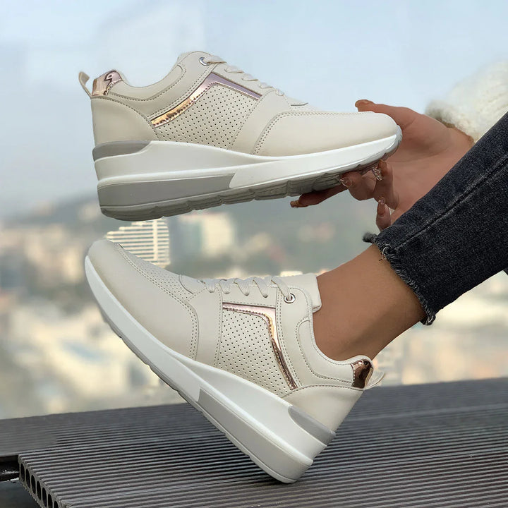 Beige platform sneakers with rose gold accents, worn with dark jeans on outdoor bench