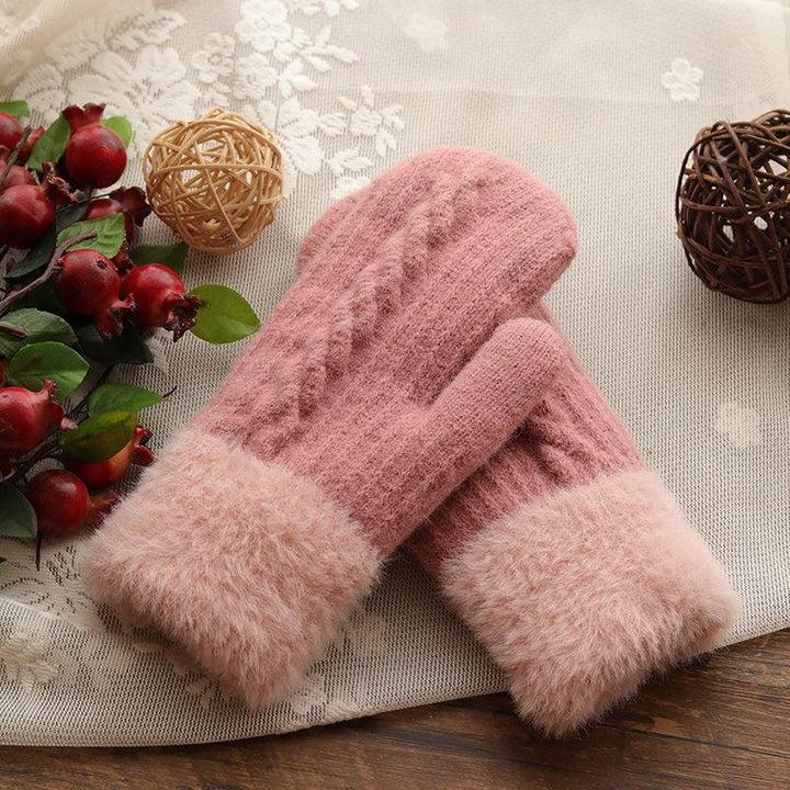 Soft pink knit wool mittens with fluffy cuffs on lace tablecloth beside decorative dried red berries and wicker balls