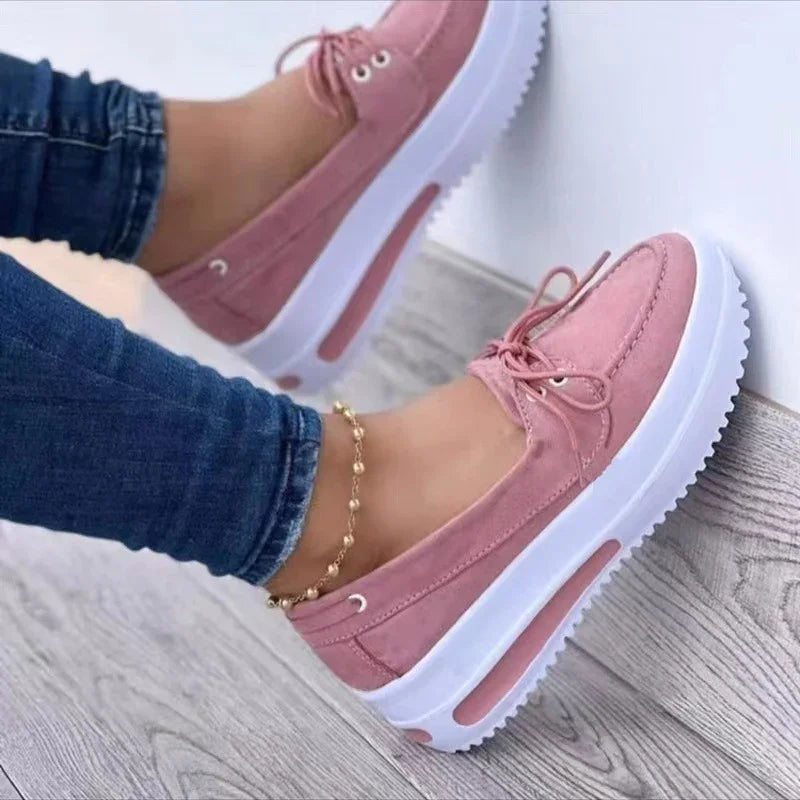 Pink women’s platform sneakers with white soles worn with blue jeans and gold anklet on wooden floor