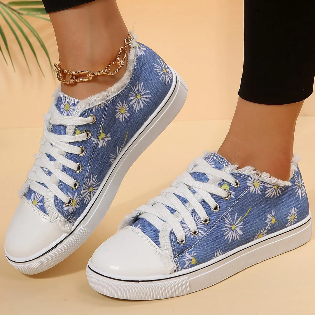 Blue denim sneakers with white daisy print, frayed edges, white laces, and rubber soles