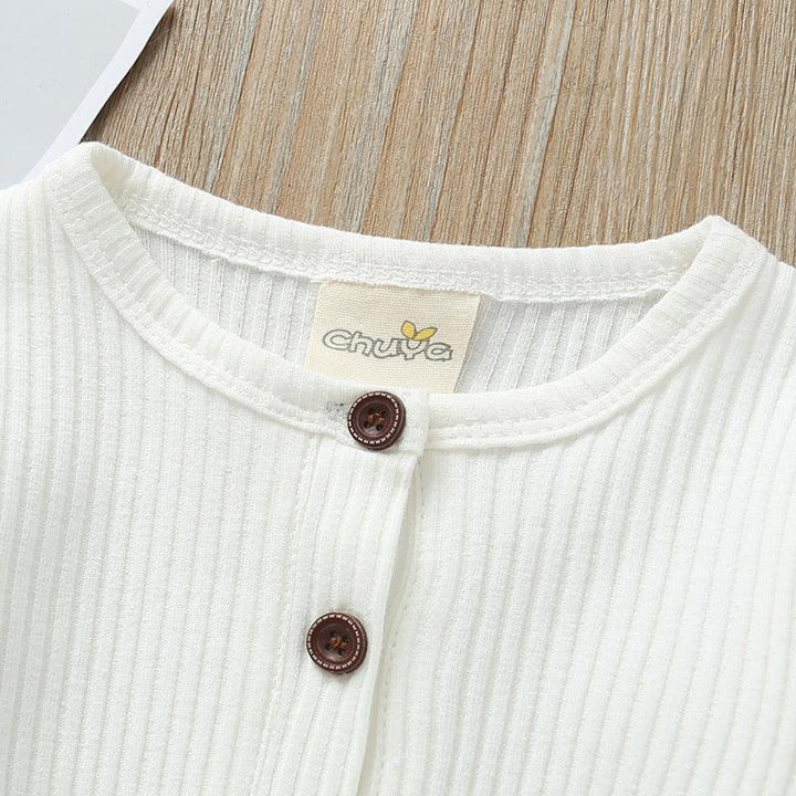 Close-up of white ribbed fabric top with round neckline and brown buttons on wooden surface