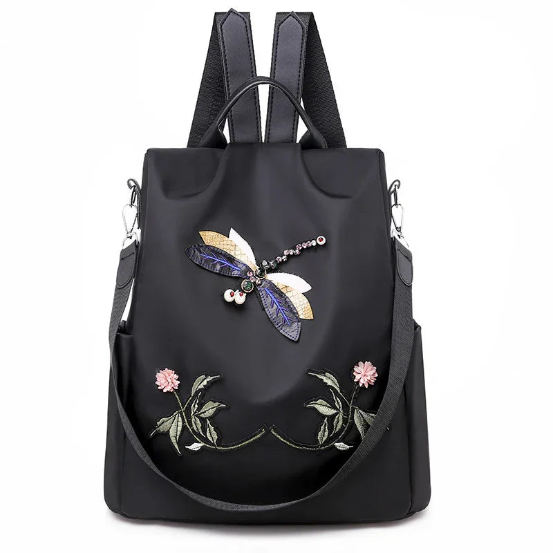 Black backpack with embroidered dragonfly and floral design, featuring detachable shoulder strap and top handle