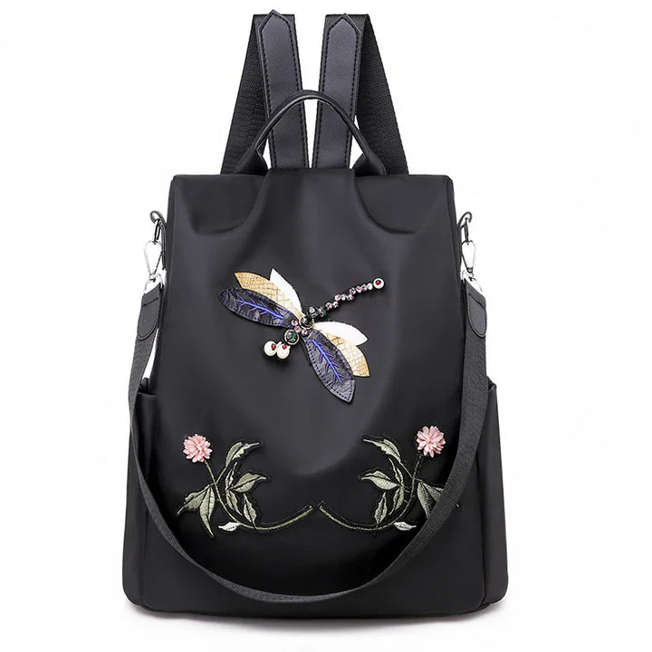 Black backpack with embroidered dragonfly and floral design, featuring detachable shoulder strap and top handle
