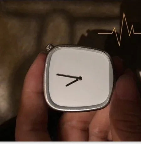 Close-up of a hand holding a modern, square silver wristwatch with a minimalist white dial and black hour and minute hands