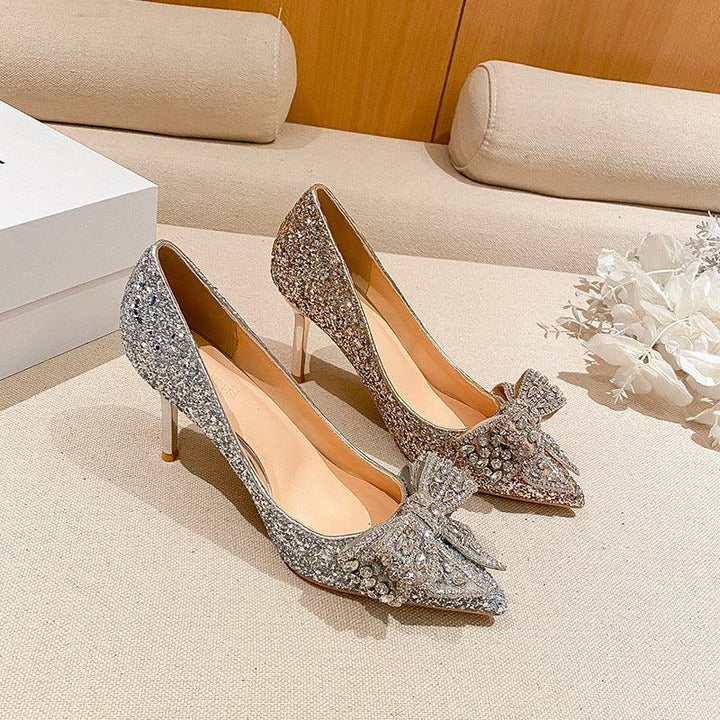 Pair of glittery high-heeled pumps with jeweled bow decorations on beige fabric surface