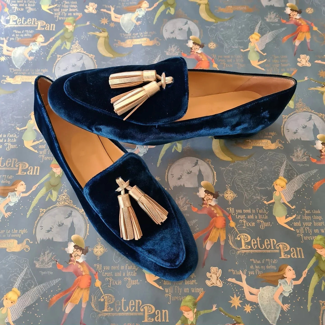Pair of navy blue velvet loafers with gold tassels on a Peter Pan themed background
