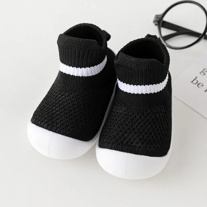 Black and white baby sock sneakers with knitted fabric and white soles on white background