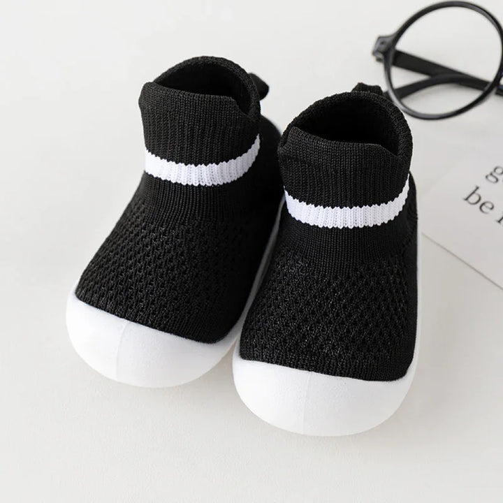 Black and white baby sock sneakers with knitted fabric and white soles on white background