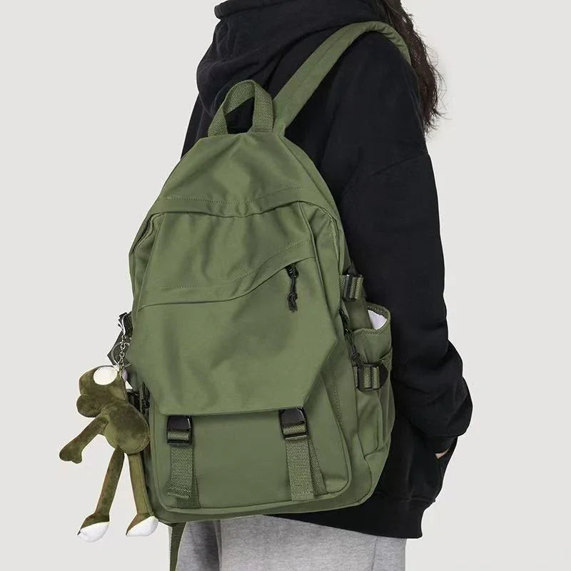 Person wearing black hoodie and gray pants carrying green backpack with plush frog keychain