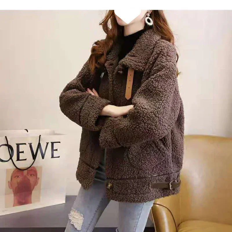 Woman wearing oversized brown sherpa fleece jacket with leather buckle details, paired with ripped jeans