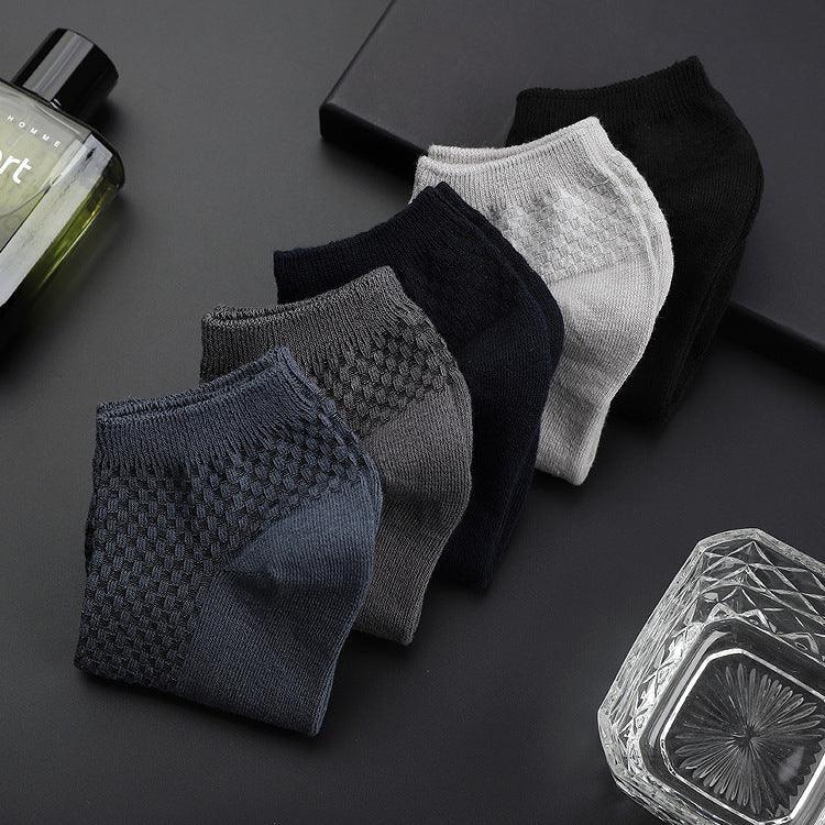 Set of five textured ankle socks in navy, gray, black, and white on a black surface with cologne and glass