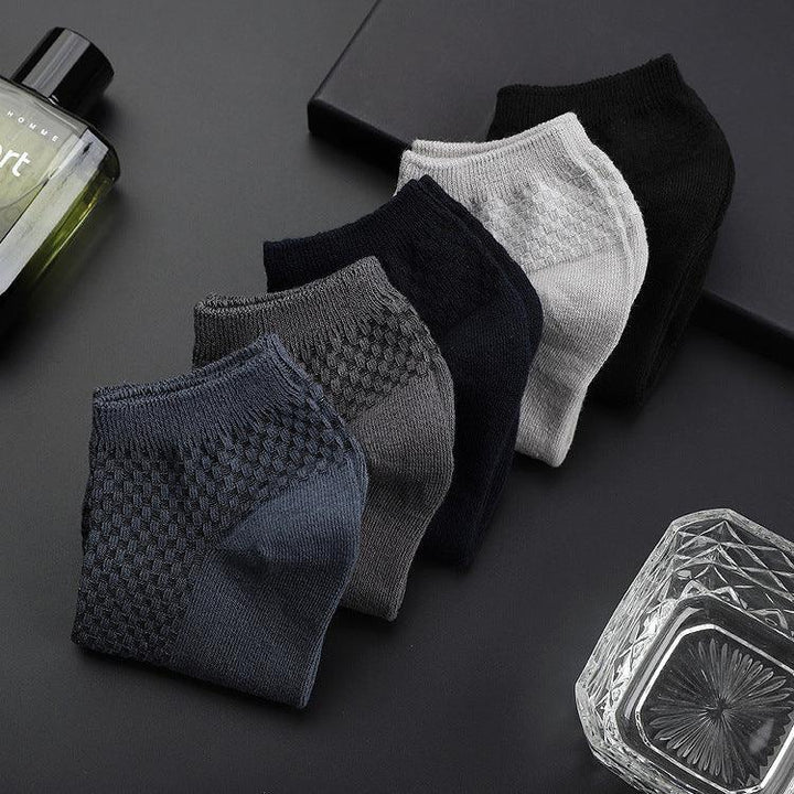 Set of five textured ankle socks in navy, gray, black, and white on a black surface with cologne and glass