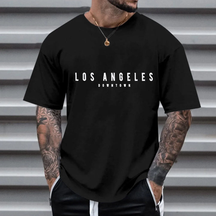 Man wearing black Los Angeles Downtown graphic t-shirt with tattooed arms and necklace