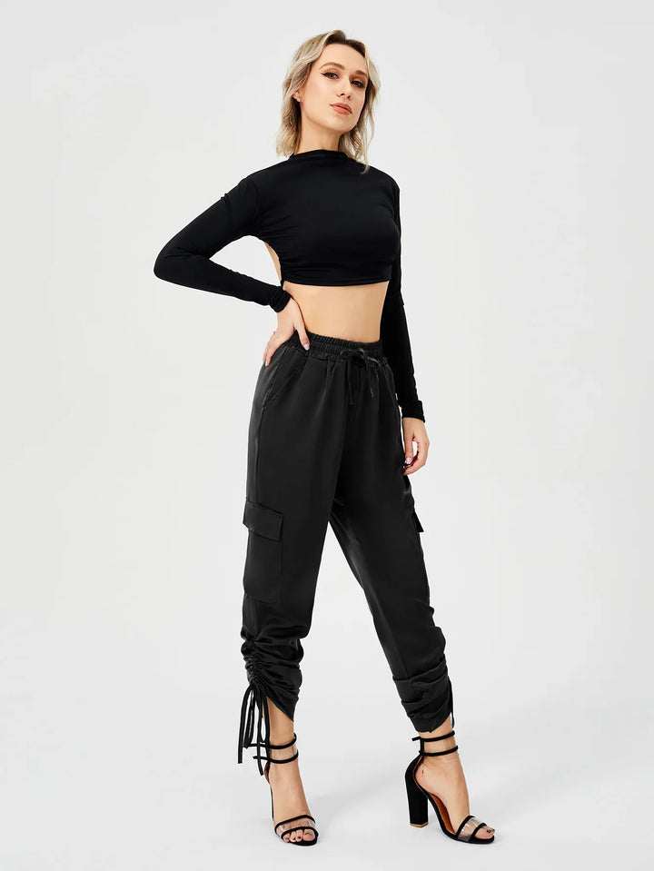 Woman wearing black long-sleeve crop top and ruched black cargo pants with ankle-tie heels