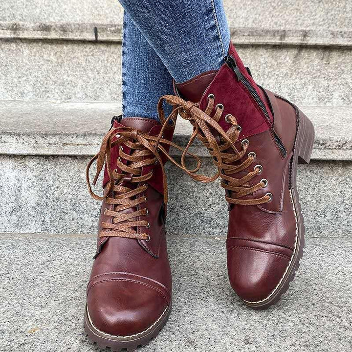 Close-up of burgundy leather ankle boots with brown laces and side zipper worn with blue jeans on stone steps