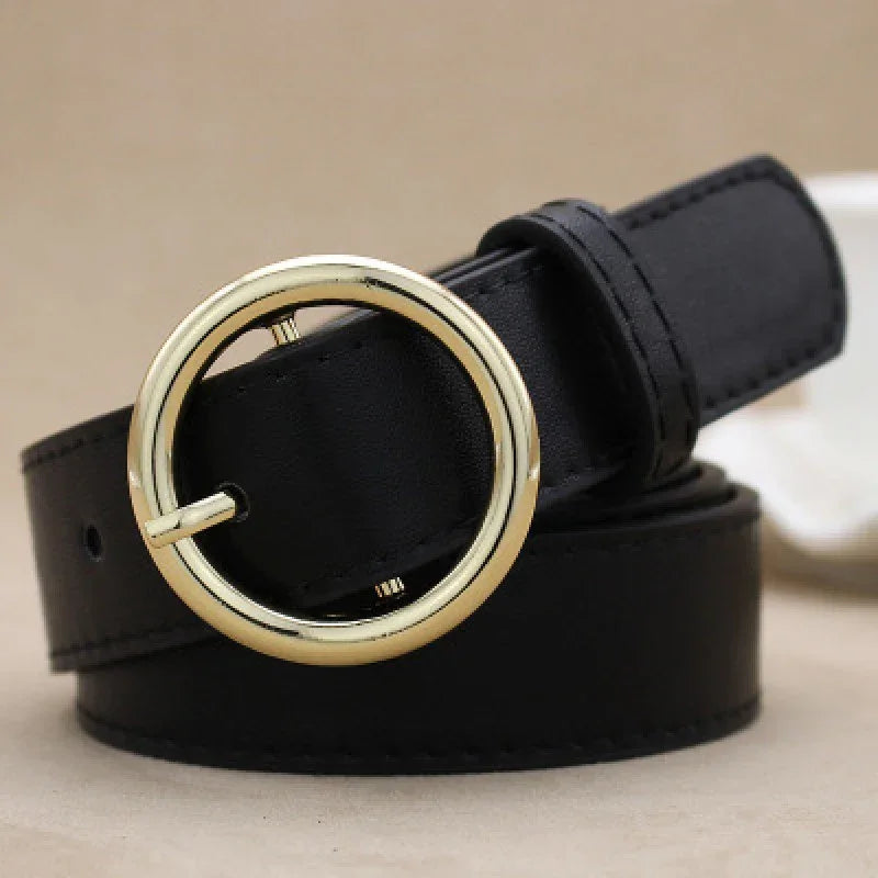 Black leather belt with a round gold buckle on a beige background