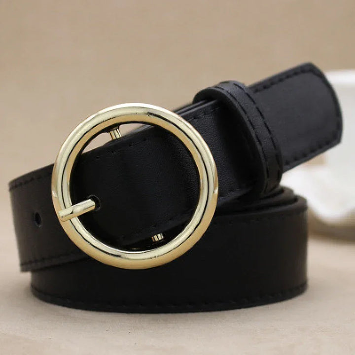 Black leather belt with round gold buckle on beige background