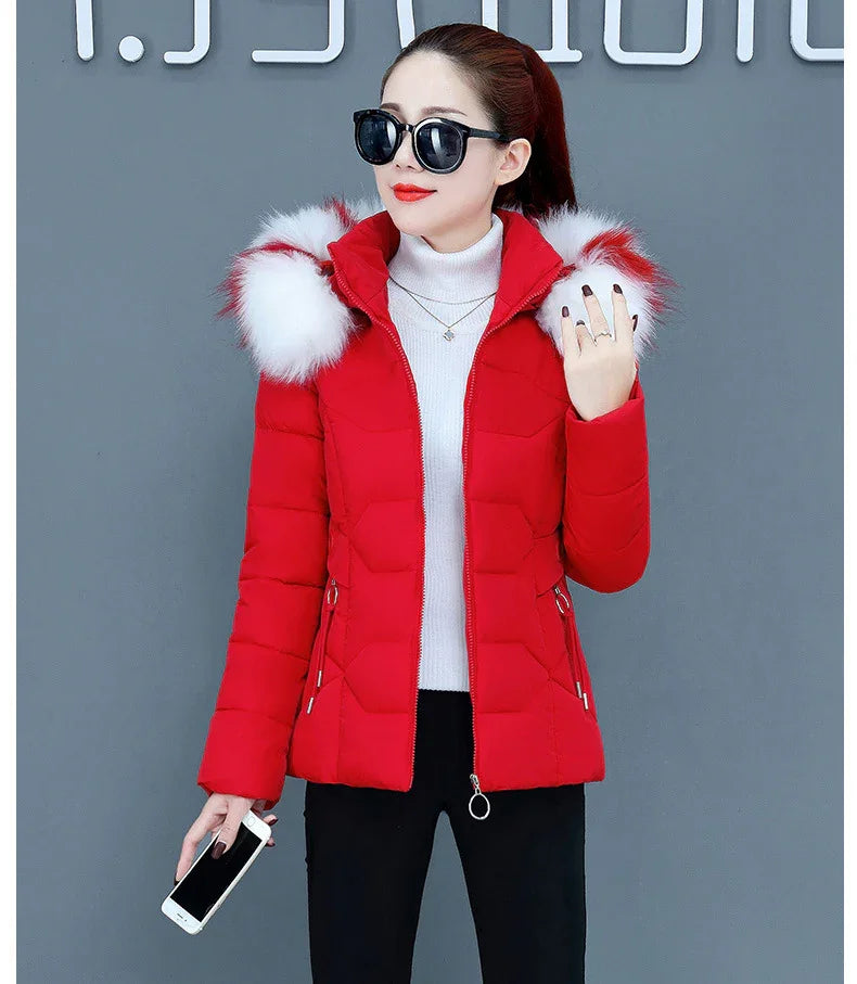 Woman wearing red padded winter jacket with white fur trim hood, black sunglasses, and holding a smartphone