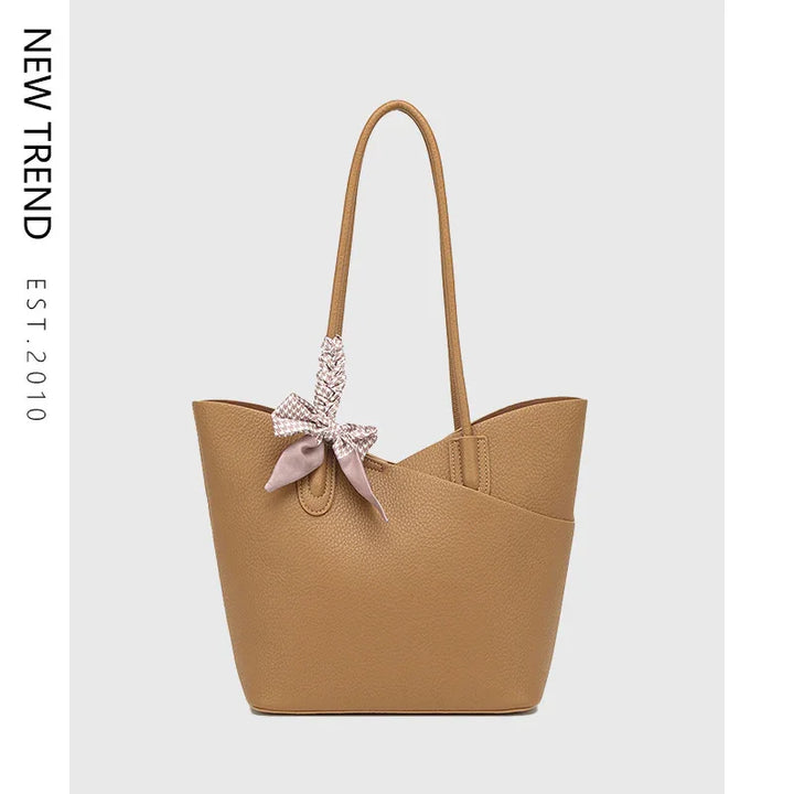Tan leather tote bag with long handles and decorative patterned bow on neutral background